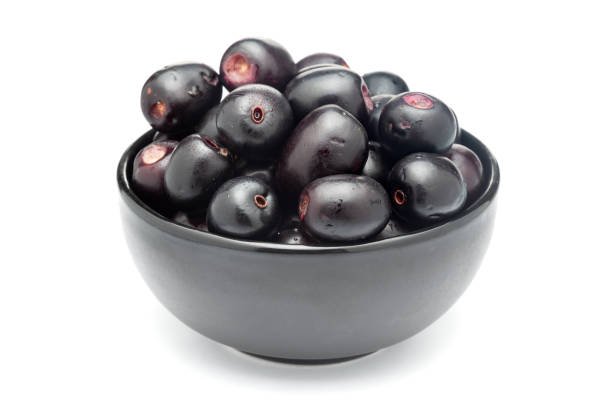 A black ceramic bowl filled with 'Indian blackberry' or Jamun (Syzygium cumini) fresh fruits. Isolated on a white background. Front view.