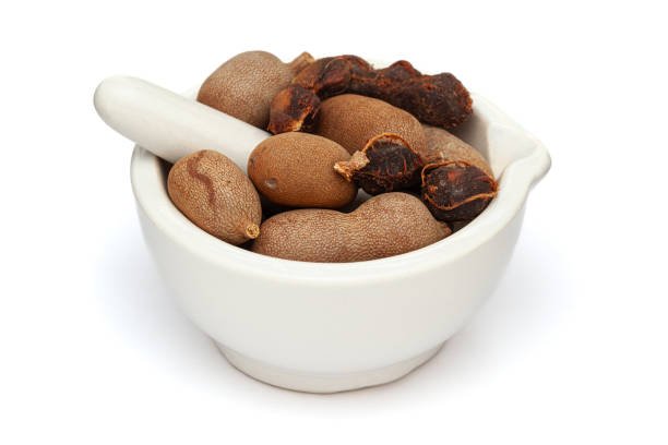 Close-up of fresh Organic Sweet Tamarind (Tamarindus indica) Fruit, in white ceramic mortar and pestle, isolated on a white background.